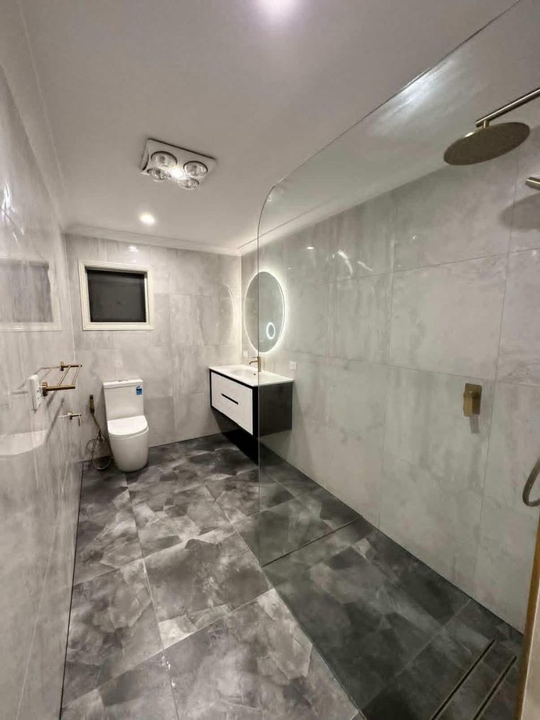 Same bathroom after renovation with a walk-in shower, marble-look walls and charcoal floor tiles