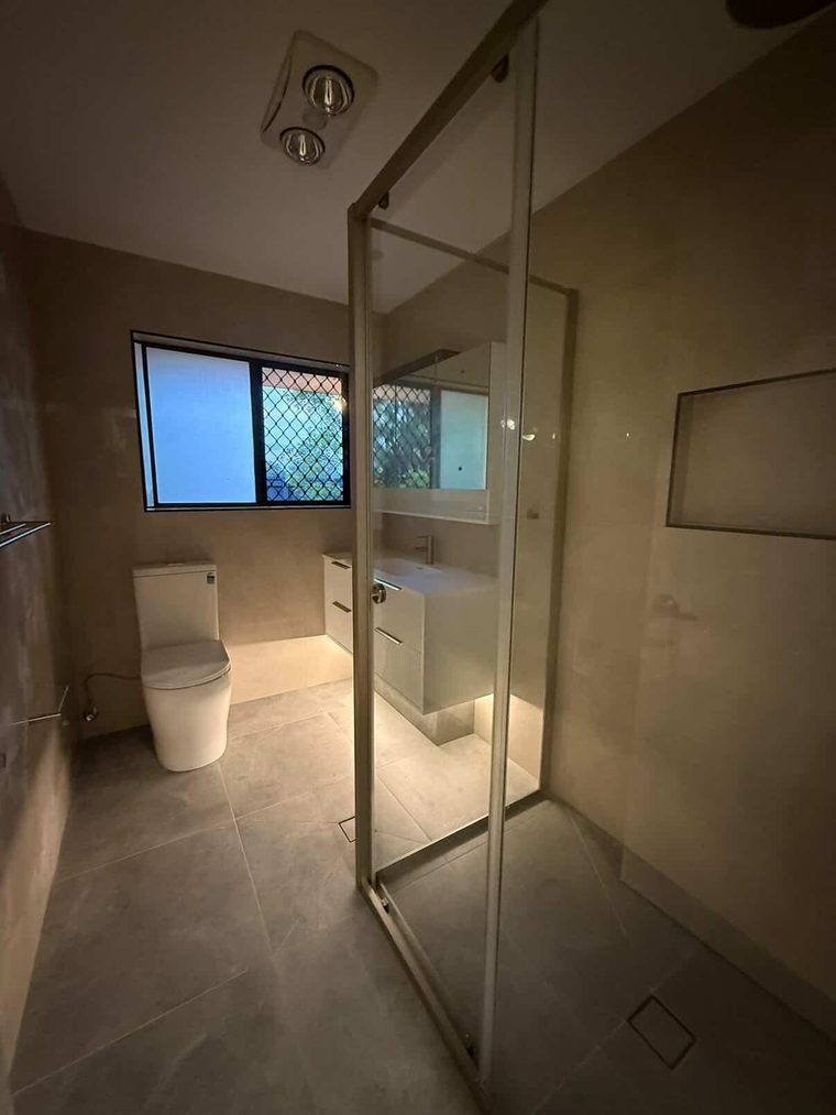 Same bathroom after renovation with a frameless shower, wall-hung vanity and stone-look tiling