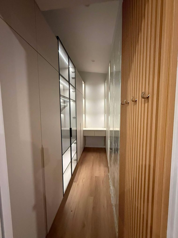 Walk-in robe with floor-to-ceiling joinery, glass-front cabinetry and a timber batten feature wall