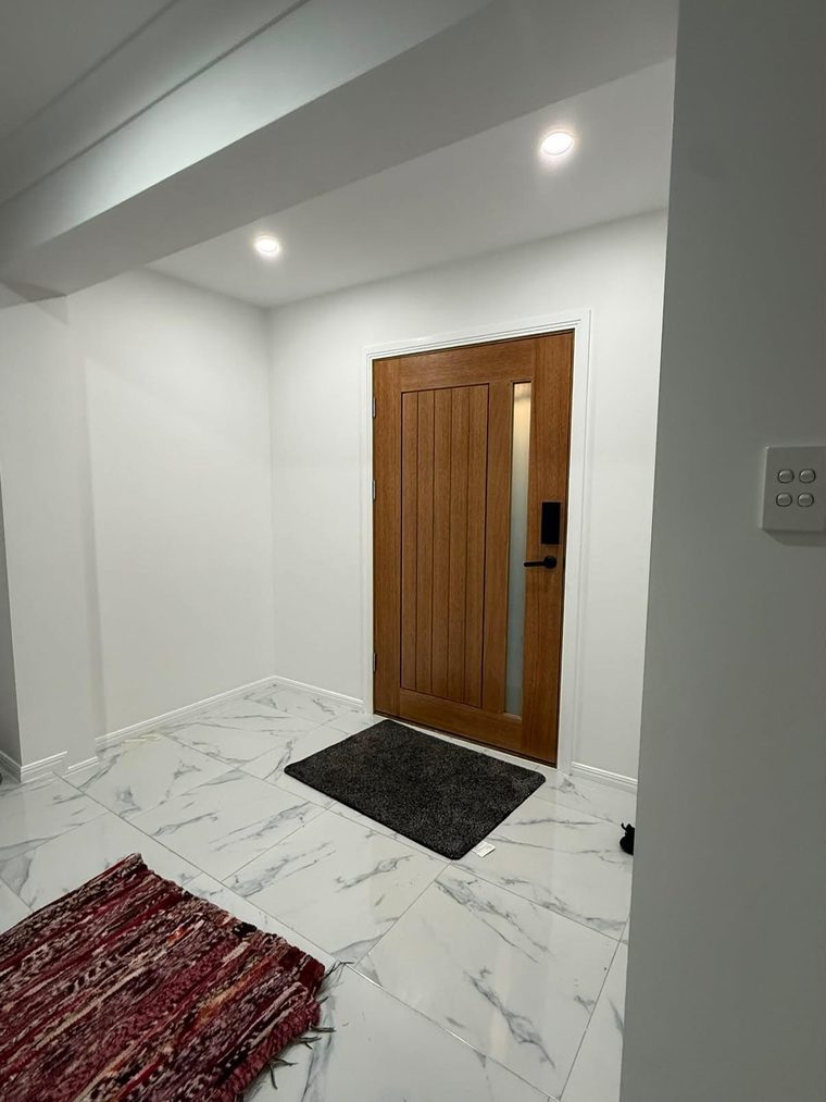 Same entry hallway after renovation with rendered walls, large-format tiles and a new timber door