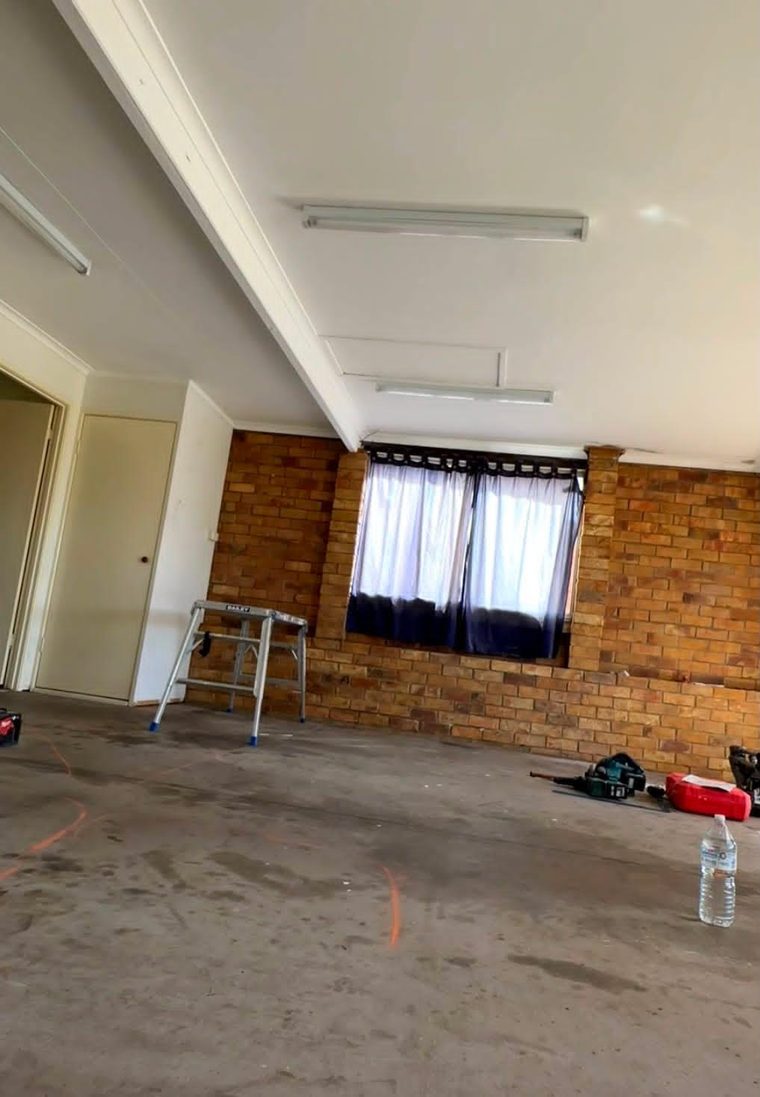 Garage before conversion, with a bare slab, unlined brick wall and fluorescent battens