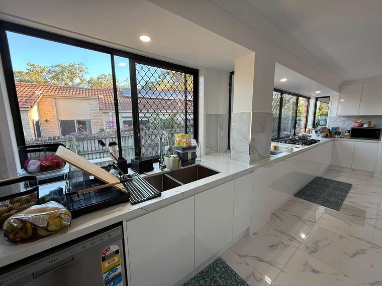 Same kitchen after renovation with a long stone benchtop, new joinery and large-format floor tiles