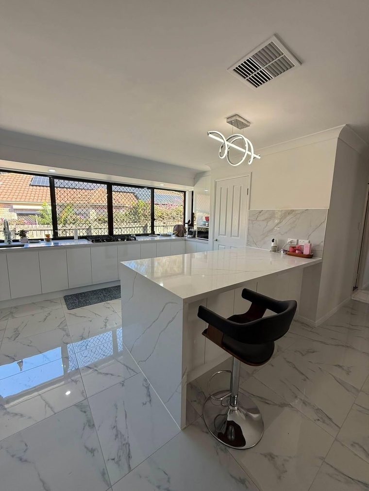 Renovated kitchen with a waterfall-edge stone island, breakfast seating and marble-look floor tiles