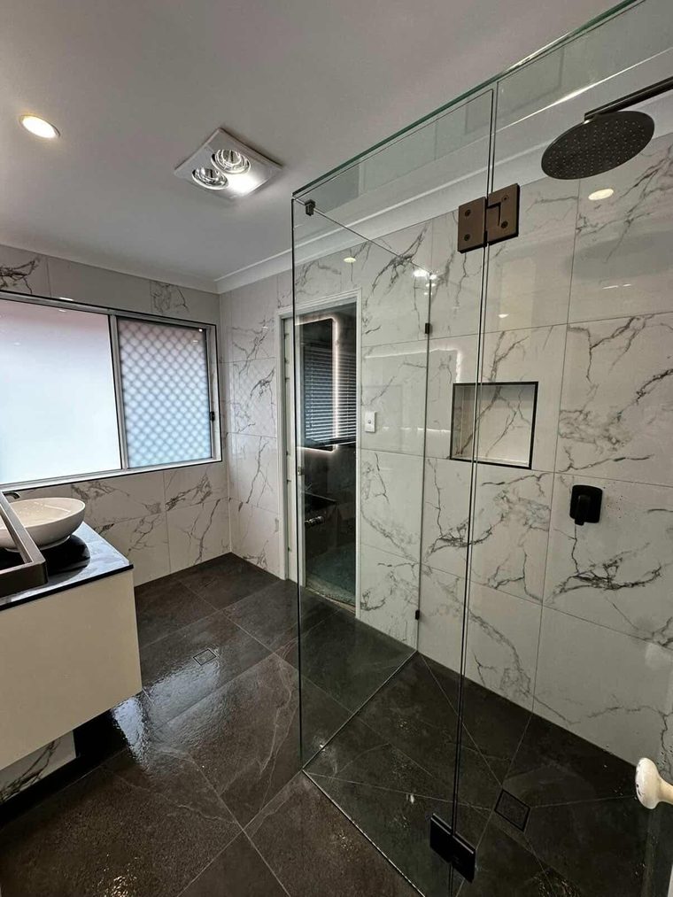 Frameless glass shower with marble-look wall tiles and a rain shower head