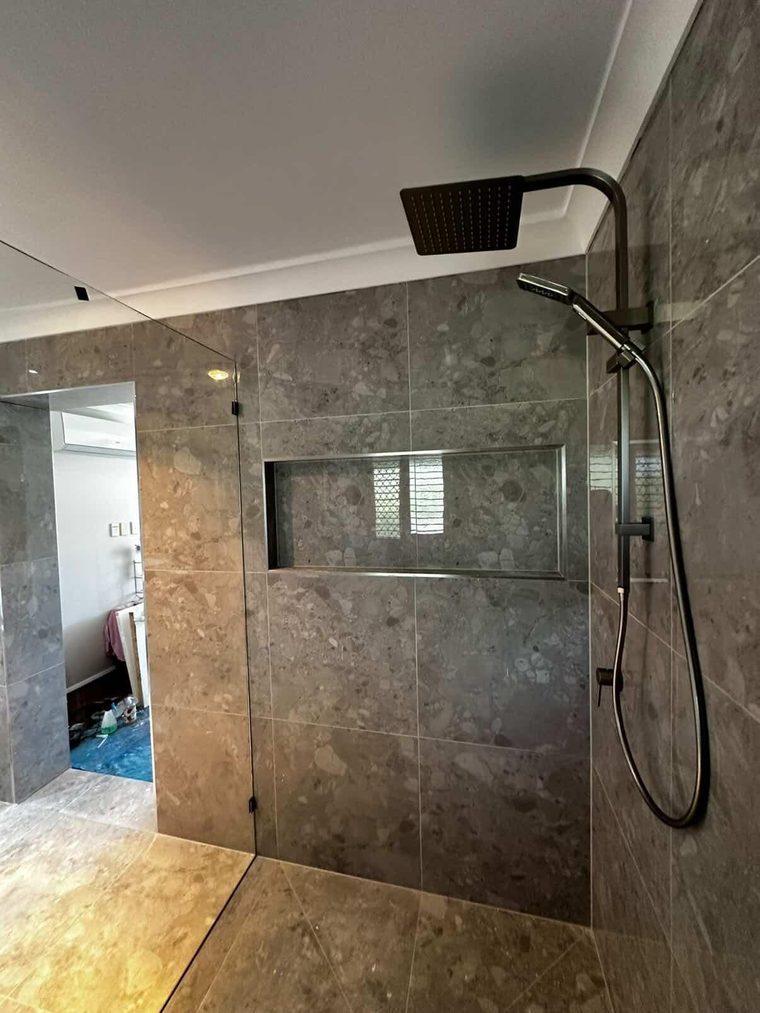 Walk-in shower with stone-look tiling, matte black rail shower and adjoining timber flooring