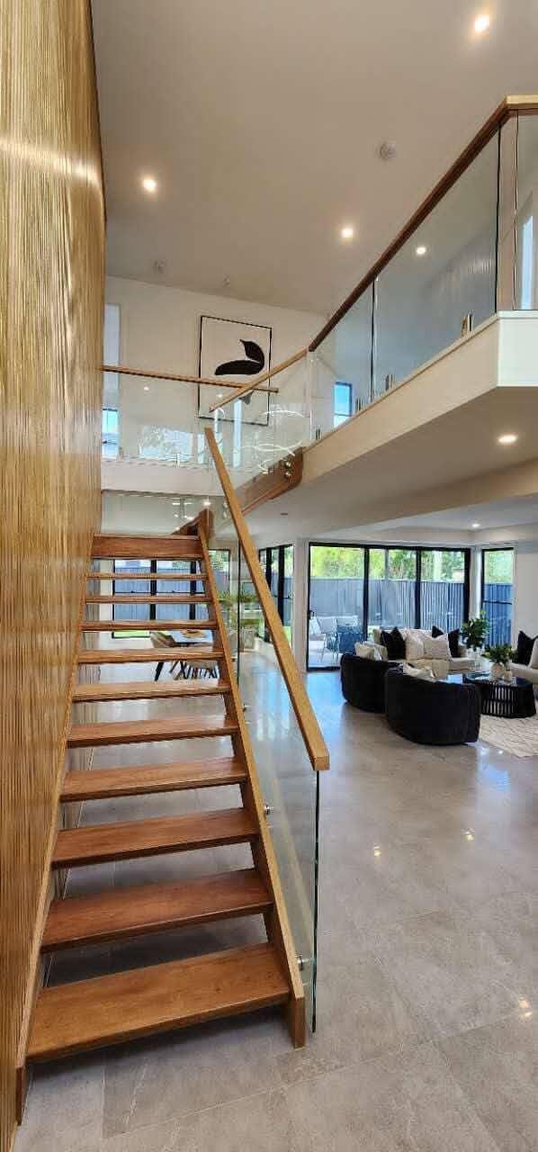 Custom timber staircase with a frameless glass balustrade in a double-height void